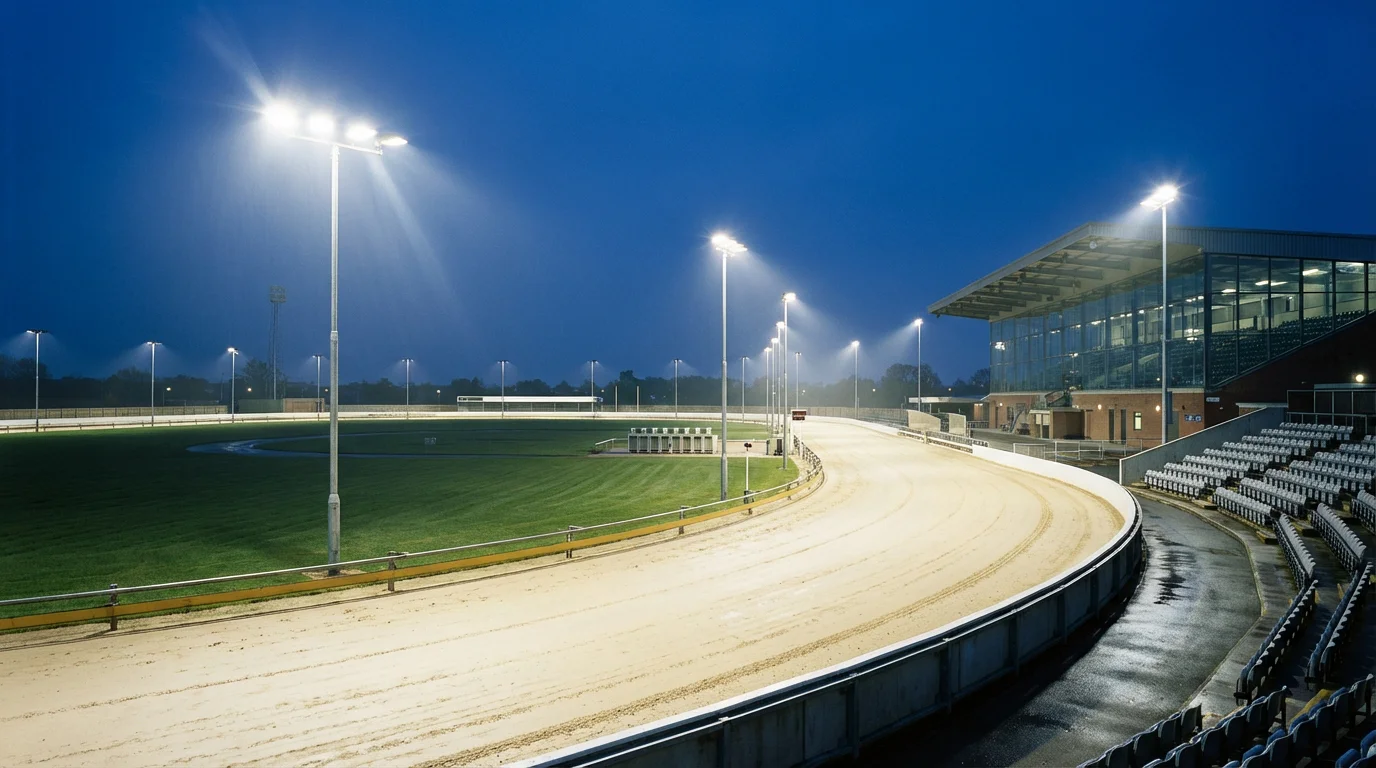 Floodlit greyhound racing stadium in the UK with sand track and empty traps at dusk